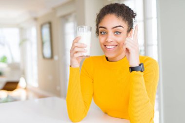 Genç Afrikalı Amerikalı kadın taze süt bir bardak içme bir fikir veya soru mutlu yüz, bir numara ile parmak işaret ile şaşırttı