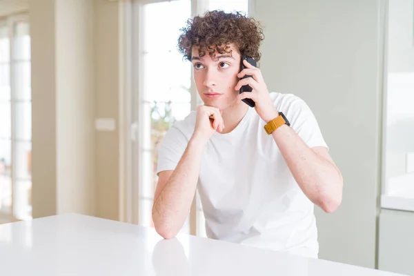 Jonge Man Praten Telefoon Thuis Serieus Gezicht Denken Vraag Zeer — Stockfoto