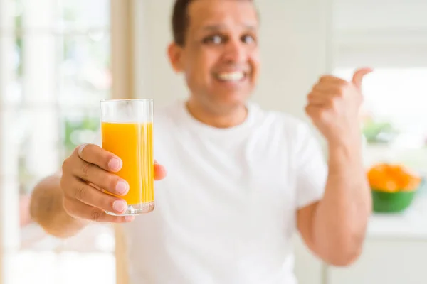 中年男子在家里喝一杯橙汁指着 用大拇指向一边露出开心的脸微笑 — 图库照片