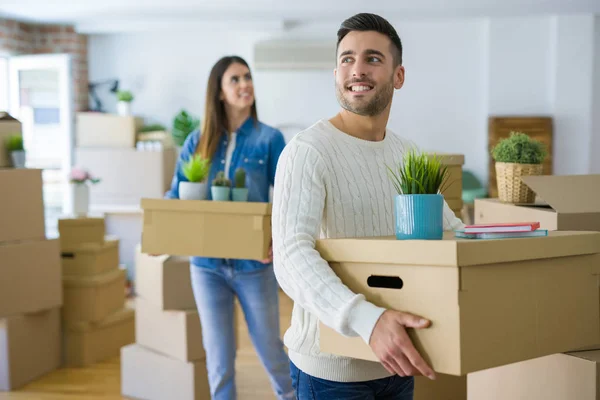 Young couple moving to a new home, smiling happy holding cardboard boxes at new apartment
