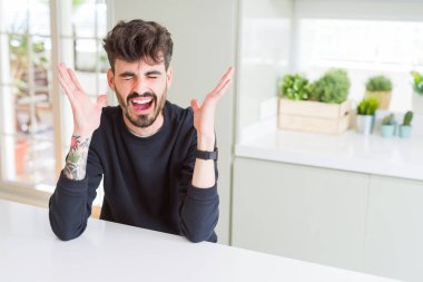 Beyaz masada oturan rahat sweatshirt giyen genç adam silah ile başarı için deli ve çılgın kutluyor ve heyecanlı çığlık kapalı gözleri kaldırdı. Kazanan kavramı