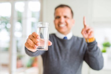 Orta yaş adam evde su bardak içme mutlu yüz, bir numara ile bir fikir ya da soru işaret parmağı ile şaşırttı
