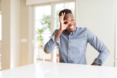 Yakışıklı afro-amerikan adam beyaz masada el gülümseyerek ok jest yapıyor, mutlu yüz ile parmakları ile bakarak göz.