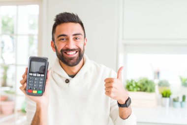 Yakışıklı İspanyol adam satış noktası terminal dataphone büyük bir gülümseme ok işareti yapıyor mutlu tutan, parmakları ile başparmak, mükemmel işareti