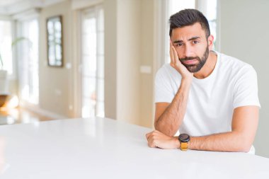 Yakışıklı İspanyol adam evde rahat beyaz t-shirt yorgun görünümlü ve çapraz kolları ile depresyon sorunları ile sıkılmış düşünme.