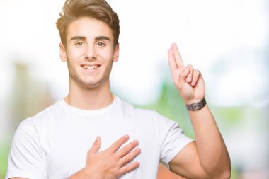 Beyaz t-shirt üzerinde izole giyen genç yakışıklı adam arka plan Swearing göğüs ve parmaklar, el ile bir sadakat sözü yemin yapma