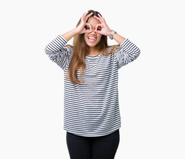 Giyen genç güzel esmer kadın kazak dilini, parmaklarının arasından baktığını yapışmasını dürbün gibi ok jest yapıyor izole arka plan üzerinde çizgili. Deli ifade.