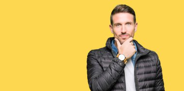 Yakışıklı adam emin çapraz kollar ve çeneme kaldırdı el ile gülümseme ile kameraya bakarak kış palto giyiyor. Pozitif düşünce.