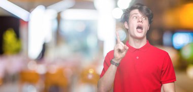 Başarılı fikirle izole arka plan işaret parmağı üzerinde kırmızı t-shirt giyen genç yakışıklı adam. Çıktıktan ve mutlu. Bir numara.