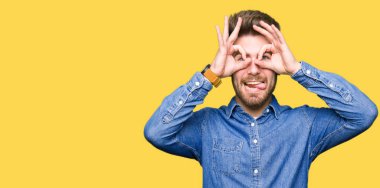 Rahat denim gömlek giyen genç yakışıklı sarışın adam dürbün yapışması gibi ok jest yapıyor, gözleri parmaklarla bakıyor. Çılgın ifade.