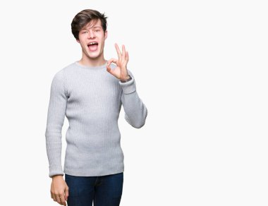 İzole arka plan el ve parmaklar ok işaretiyle yapıyor olumlu gülümseyen üzerinde kış kazak giyen genç yakışıklı adam. Başarılı ifade.