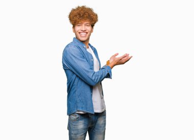 Genç yakışıklı adam ile afro saç giyen denim ceket el ve açık palmiye ile yan Işaret, reklam gülümseyen mutlu ve emin sunan