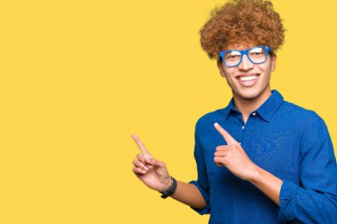 Gülümseyen ve iki elleri ve parmakları ile tarafına işaret kamera bakarak mavi gözlük takan afro saçlı Genç yakışıklı adam.