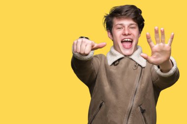 İzole arka plan üzerinde kış ceket giyen genç yakışıklı adam gösteren ve parmak numarası altı ile işaret kadar güven ve mutlu gülümseyen.