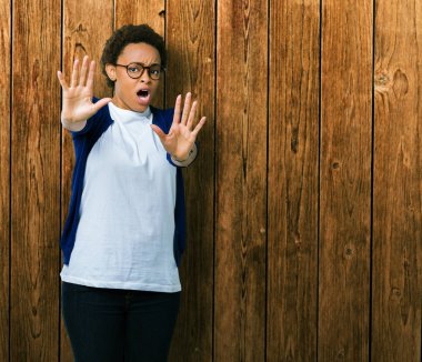 Şokta bağırarak korkuyor ve dehşet korku ifade dur hareketi el ile ile izole arka plan üzerinde gözlük takan genç güzel Afrikalı-Amerikalı kadın. Panik kavramı.