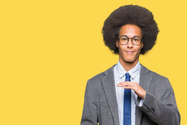 Young african american business man with afro hair wearing glasses gesturing with hands showing big and large size sign, measure symbol. Smiling looking at the camera. Measuring concept.