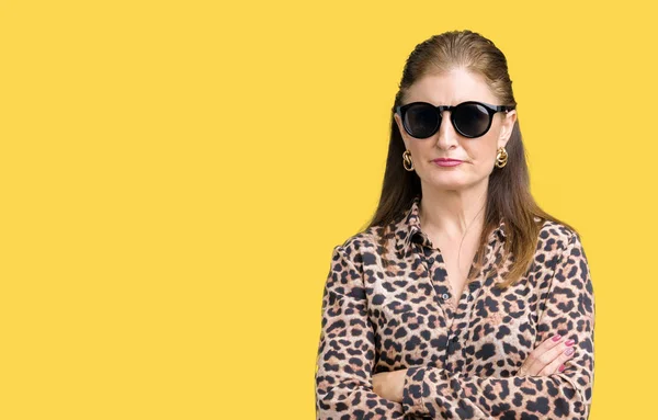 Middle age mature rich woman wearing sunglasses and leopard dress over isolated background skeptic and nervous, disapproving expression on face with crossed arms. Negative person.