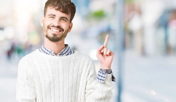 カメラを見て側に手と指で指しての顔に大きな笑みを浮かべて隔離された背景に冬のセーターを着ている若いハンサムな男 — ストック写真