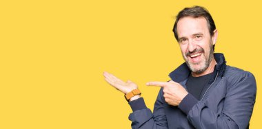 Hayret ve el ile sunulması ve parmak ile işaret ederken kameraya gülümseyen bir ceket giyen orta yaş yakışıklı adam.