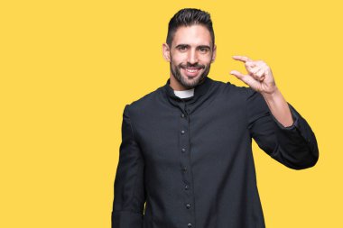 Genç Hıristiyan rahip izole arka plan gülümseyen ve süre seyir ve kamera boyutu işaret parmaklarıyla yapıyor el ile kendinden emin eller üzerinde. Ölçü kavramı.