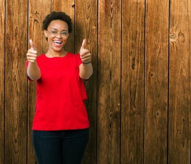 Güzel genç Afro-Amerikan kadın gözlük izole arka plan onaylama üzerinde el ile pozitif jest yapıyor gülümseyen ve başarı için mutlu başparmak. Kamera, kazanan jest arıyorsunuz.