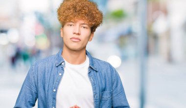 Afro saçlı kot giyen genç yakışıklı adam ceket el ele tutusun ve rahat ve neşeli gülümseyen parmak çarpı işareti. Başarı ve iyimser