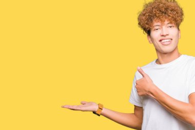 Casual beyaz t-shirt gösteren giyen afro saçlı yakışıklı delikanlı palm el ve yukarıya, mutlu ve neşeli gülümseyen baş parmakları Tamam jest yapıyor