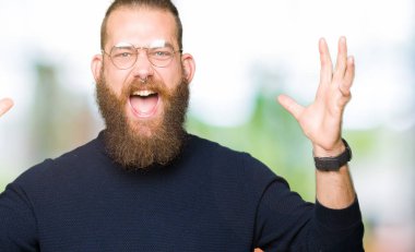 Genç sarışın adam giyen gözlük ve balıkçı yaka kazak deli ve çığlık kaldırdı ve açık gözleri heyecanlı silah ile başarı için hayran kutluyor. Kazanan kavramı