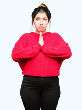 Kırmızı kazak ve ellerle birlikte AF emin gülümseyen için soran dua topuz giyen genç güzel kadın.