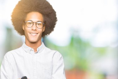 Afrikalı-Amerikalı genç afro saçlı gözlük mutlu yüz çapraz silah kameraya bakarak ile gülümseyen giyiyor. Olumlu bir kişi.