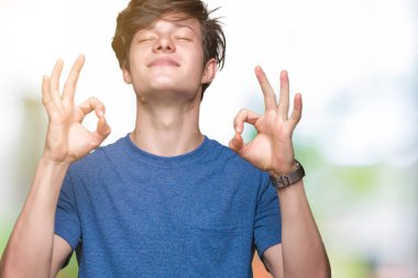İzole arka plan üzerinde mavi t-shirt giyen genç yakışıklı adam rahatla ve gülümseyen gözlerle kapalı parmak jestle meditasyon yapıyor. Yoga kavramı.
