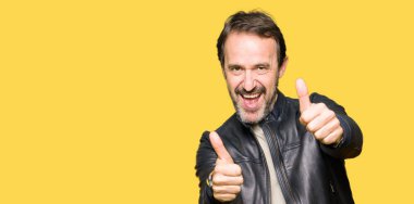 Siyah deri ceket onaylama giyen orta yaş yakışıklı adam el ile pozitif jest yapıyor gülümseyen ve başarı için mutlu yaşasın. Kamera, kazanan jest arıyorsunuz.