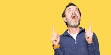 Orta yaş yakışıklı adam kazak giyiyor hayret ve yukarıya bakıp parmakları ile işaret şaşırttı ve silah kaldırdı.