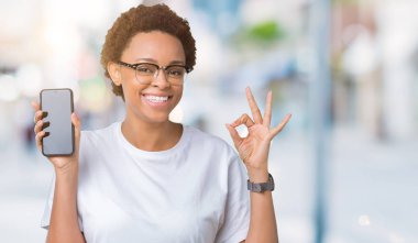 Genç Afro-Amerikan kadın gösteren smartphone ekran parmak, mükemmel sembolü ile ok işareti yapıyor izole arka plan üzerinde