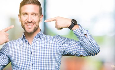 Kendinden emin gösterilen ve işaret parmakları diş ve ağız ile gülümseyen mavi gözlü yakışıklı iş adamı. Sağlık kavramı.