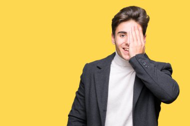 Yüz ve sürpriz duygu kendine güvenen gülümseme ile el ile bir göz kaplayan izole arka plan üzerinde kış ceket giyen genç zarif adam.