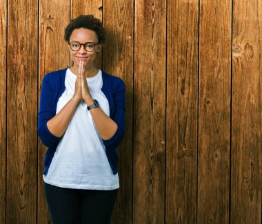 Genç güzel Afrikalı-Amerikalı kadın ellerle birlikte AF emin gülümseyen için soran dua izole arka plan üzerinde gözlük.