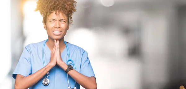 Young african american doctor woman over isolated background begging and praying with hands together with hope expression on face very emotional and worried. Asking for forgiveness. Religion concept.