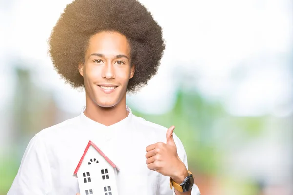 笑顔の サイン 優秀な兆候を親指をやって家を幸せに保持してアフロの髪の若いアフリカ系アメリカ人 — ストック写真