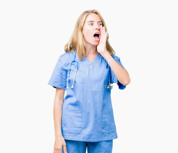 美丽的年轻医生妇女穿着医疗制服在孤立的背景大喊和尖叫的身边 手放在嘴 沟通理念 — 图库照片