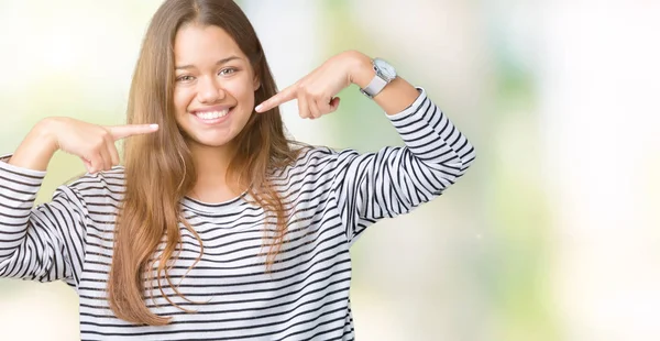 孤立した背景の上にストライプセーターを着た若い美しいブルネットの女性は 自信を持って示し 指の歯と口で指差し 健康の概念 — ストック写真