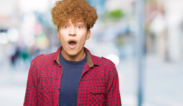Young handsome student man with afro hair wearing a jacket afraid and shocked with surprise expression, fear and excited face.