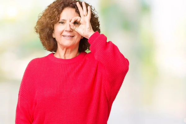 美丽的中间年龄的老年妇女红色冬季毛衣在孤立的背景做确定的手势与手微笑 眼睛通过手指看与快乐的面孔 — 图库照片