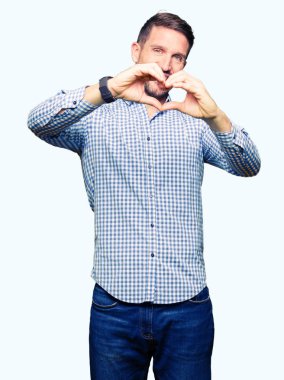 Kalp simgesi ve elleriyle şekil gösterilen aşık gülümseyen mavi gözlü yakışıklı iş adamı. Romantik kavramı.