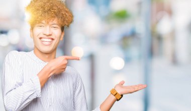 Genç yakışıklı iş adamı ile afro saç şık gömlek giyiyor hayran ve kamera gülümseyen el ile sunmak ve parmak ile işaret.