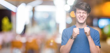 Zafer kutluyor gülümseyen izole arka kolları olan başarı için heyecan üzerinde mavi t-shirt giyen genç yakışıklı adam kaldırdı. Kazanan kavramı.