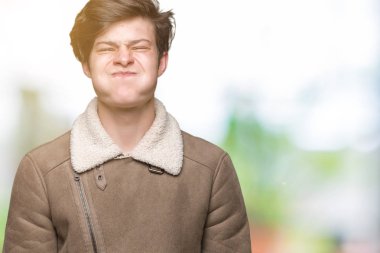 Komik surat ile yanakları şişirme izole arka plan üzerinde kış ceket giyen genç yakışıklı adam. Ağız ile hava, deli ifade şişirilmiş.