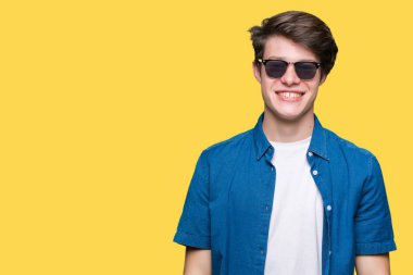 Genç yakışıklı adam yüzünde mutlu ve güzel bir gülümseme ile izole arka plan üzerinde güneş gözlüğü takıyor. Şanslı kişi.