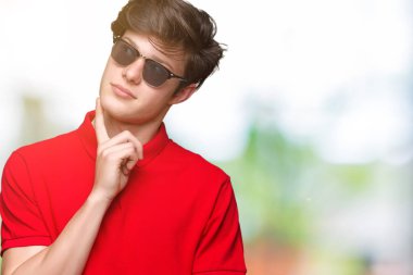 Genç yakışıklı adam çene düşünme hakkında soru, dalgın ifade üzerine el ile izole arka plan üzerinde güneş gözlüğü takıyor. Düşünceli yüzüyle gülümsüyor. Şüphe kavramı.