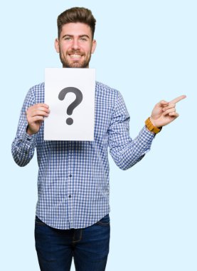Kağıt soru işareti ile çok mutlu el ve parmak ile tarafına işaret tutan genç yakışıklı adam